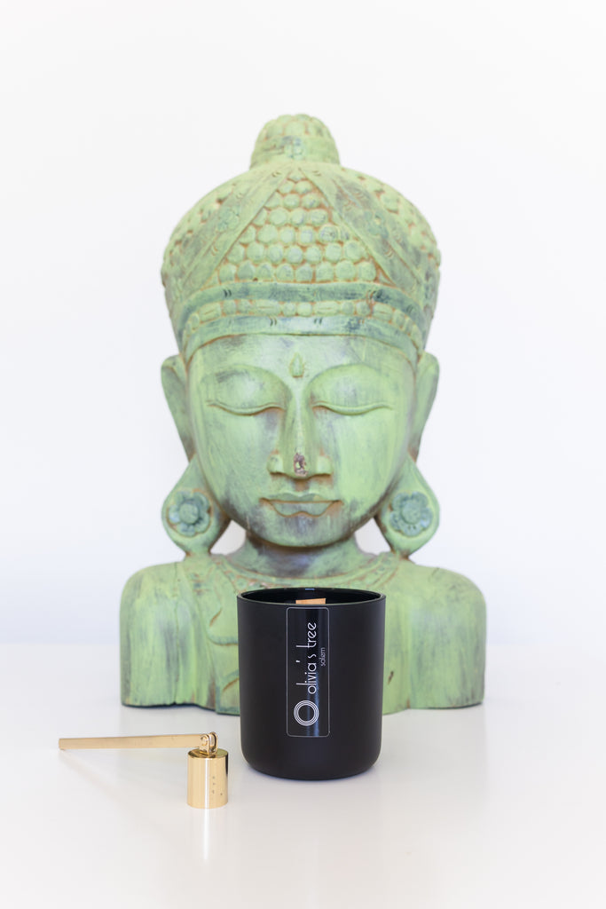 Green Buddha head and shoulders with a black candle vessel sitting in front of the Buddha with a gold candle snuffer sitting to the left of the candle. 